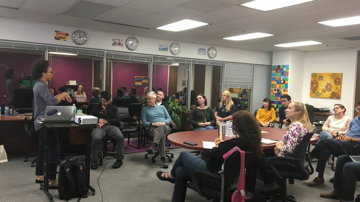 A woman giving a presentation in the Knowbility office. Attendees are seated in a circle listening to the speaker.