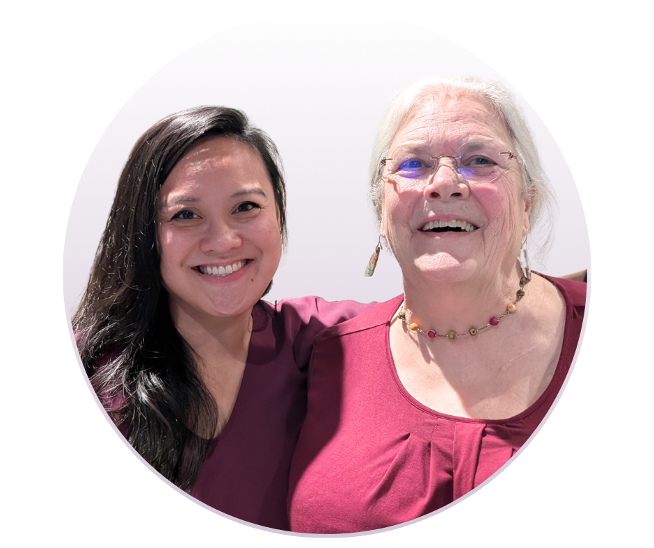 A middle aged Asian woman with long black hair standing next to a smiling Caucasian woman with color earrings and her white hair swept back in a ponytail
