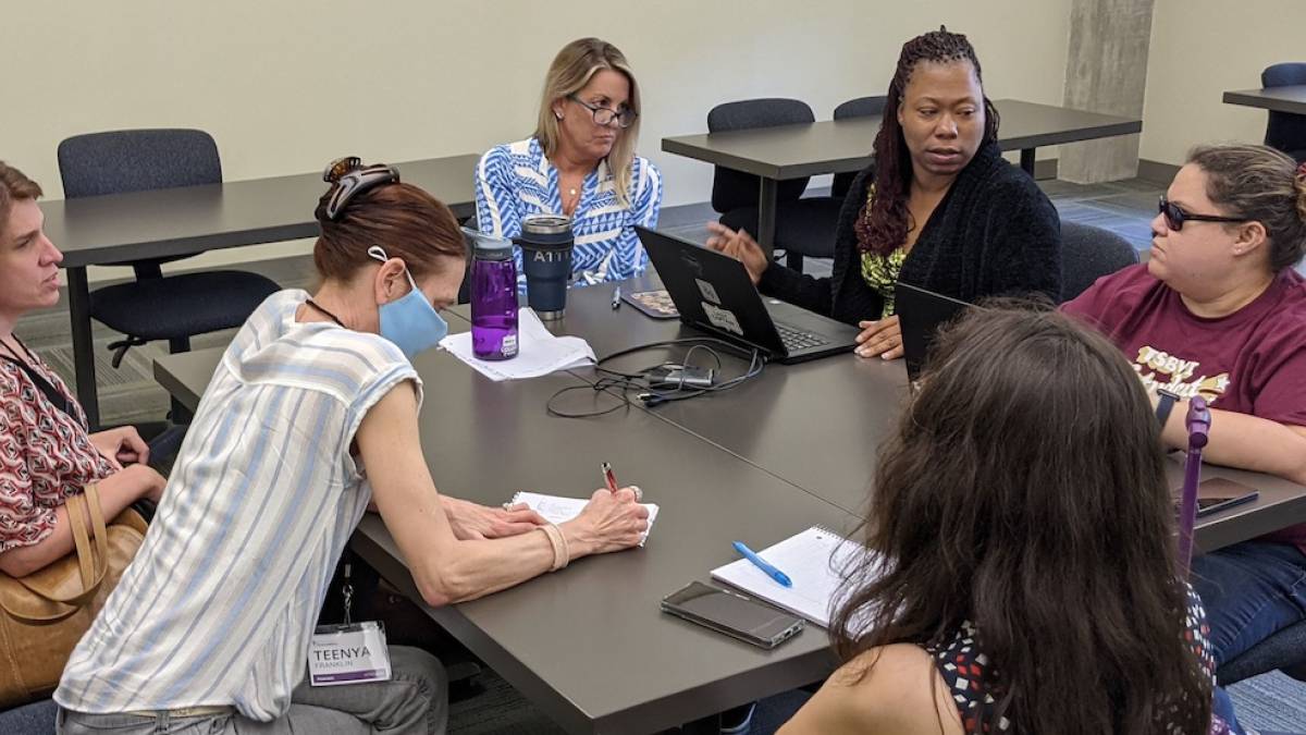 A group of attendees are gathered around a table having a discussion.