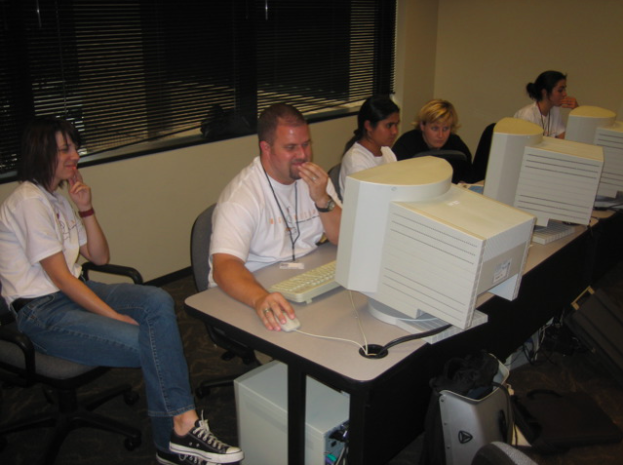 Five individuals seated around a computer, engrossed in collaborative work at the Accessibility Internet Rally (AIR). The team is focused on designing and improving a website, highlighting their dedication to web accessibility. The vintage computers in the image reflect its age, while the collective effort showcases their commitment to inclusive online experiences.