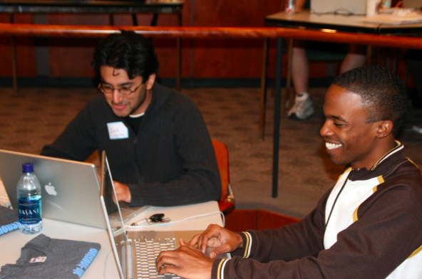 o participants engaged in collaborative work at AIR Houston 2007. Seated at a table, both individuals are engrossed in their laptops, wearing smiles of focus and camaraderie. They exemplify the spirit of teamwork and dedication during the Accessibility Internet Rally event.