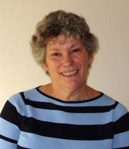 smiling woman with grey curly hair and blue and black striped shirt