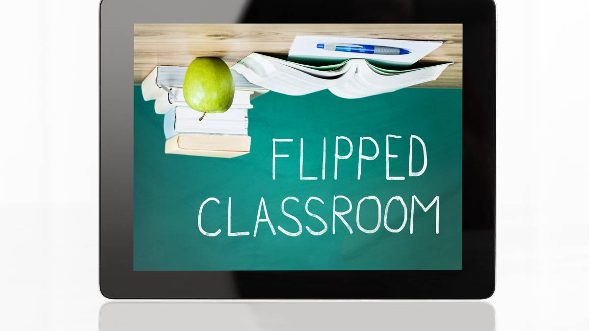 Upside desk with books and an apple above a chalkboard that reads 