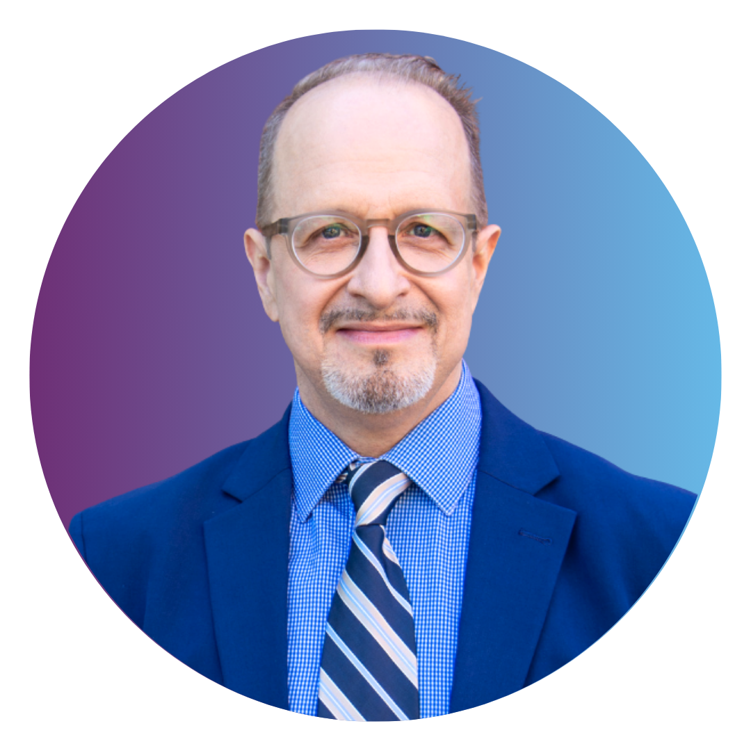 Bill Curtis Davidson is a middle aged man with gray hair and a tidy beard. He is wearing a blue suit with a blue striped tie.