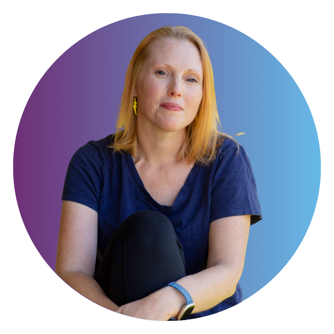 A woman with shoulder length red hair wearing a blue shirt and gold earrings