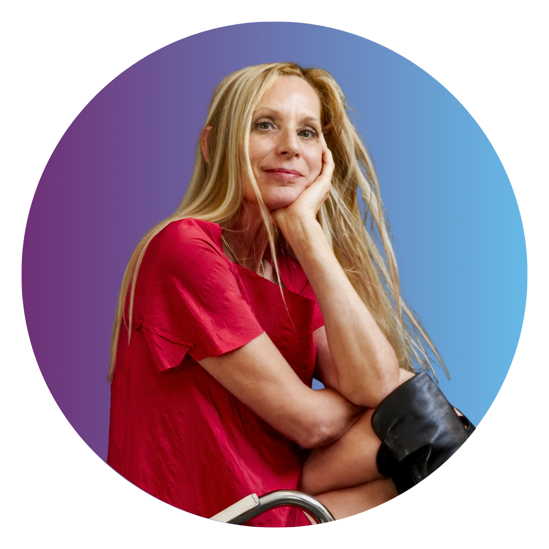 A woman with long blonde hair with her hand tucked under her chin. She wears a flowy red dress and black boots.