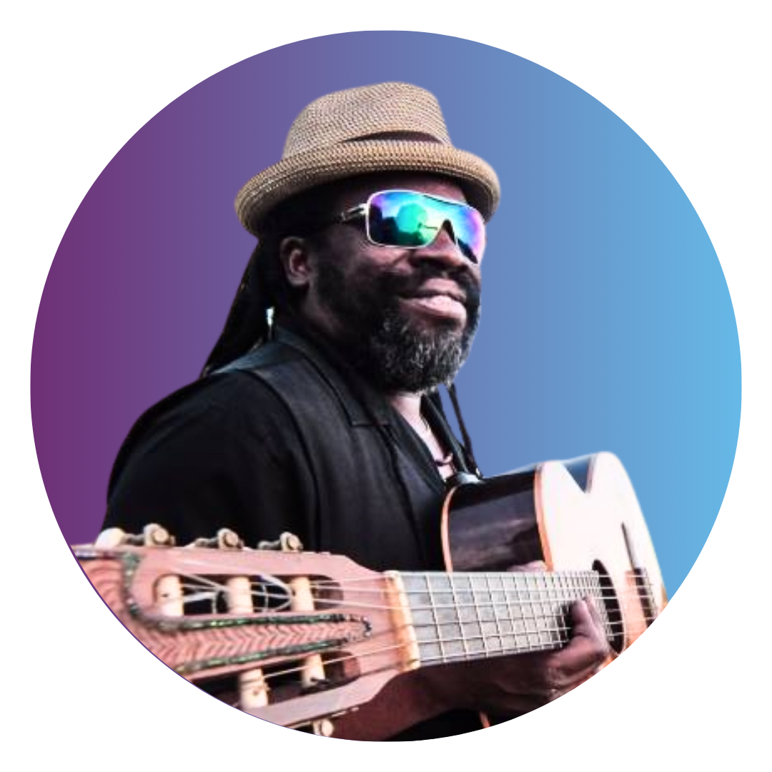 A man with long black dreadlocks wearing sunglasses and a tan fedora. He holds a bass guitar in his hands.
