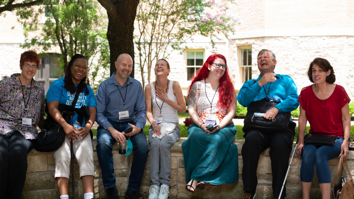A group of 7 program attendees sitting under trees smiling and laughing